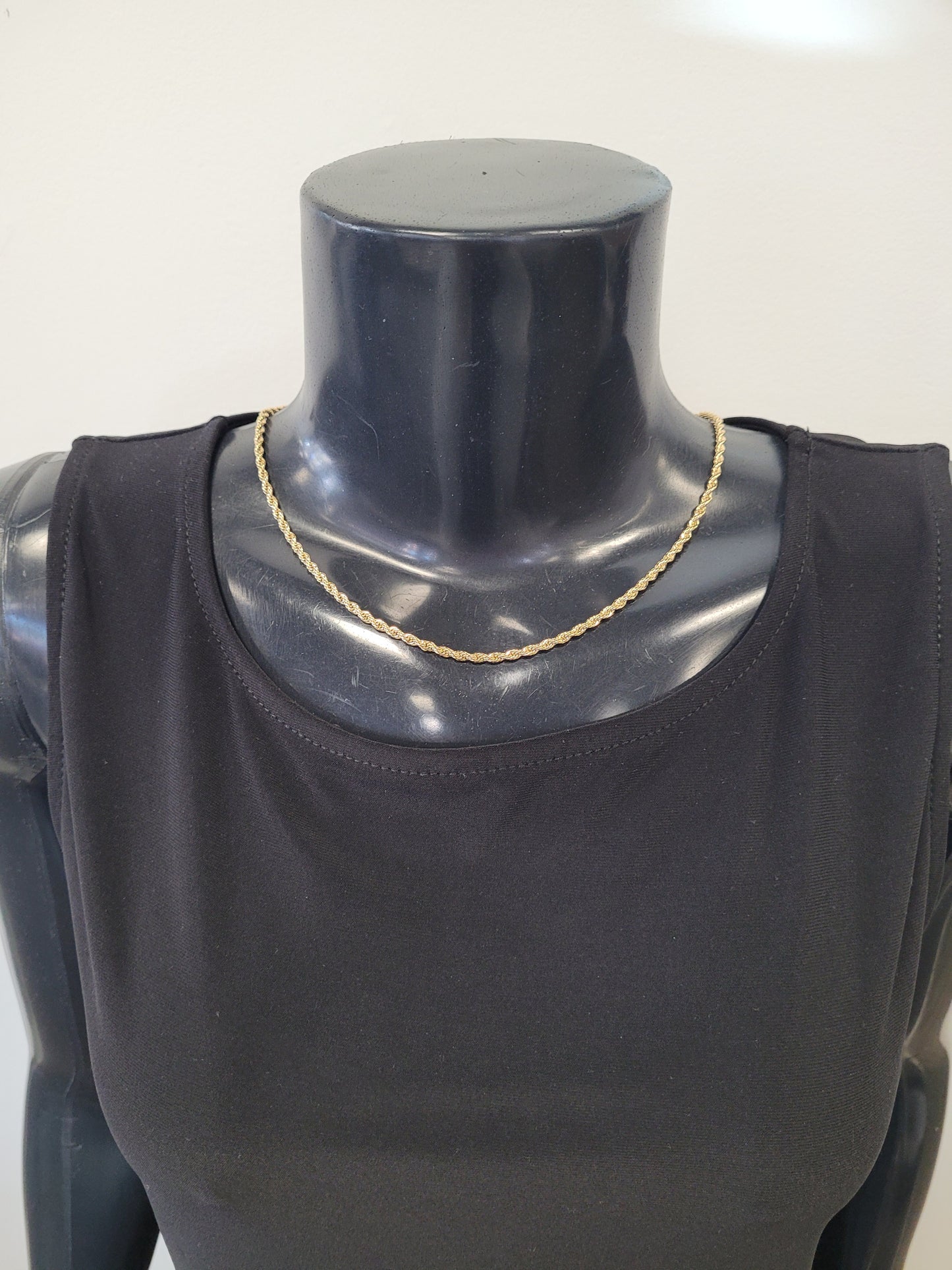 The Rhea-25 Necklace by Elise accessories, a classic gold rope chain crafted from stainless steel, is showcased on a black mannequin in a sleeveless black top, set against a plain light background.