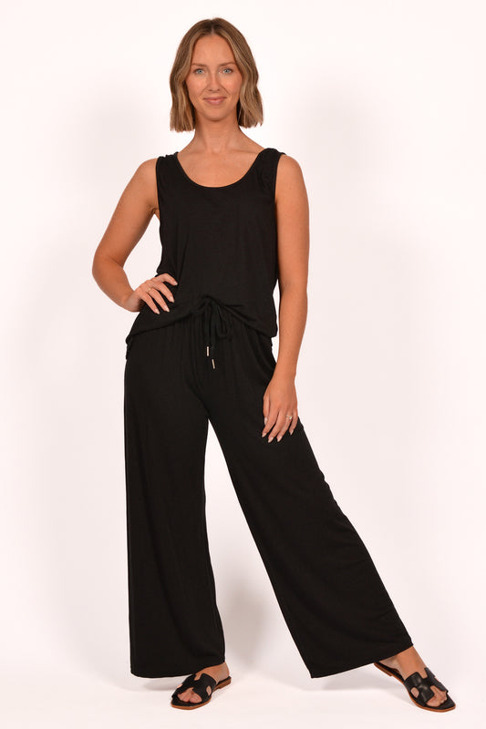 In a white backdrop, someone models the Catherine Lilywhite Drawstring Pant ITEL833011 ensemble, showcasing a sleek sleeveless black top with a waist drawstring and matching wide-leg pants. Their shoulder-length hair and black sandals enhance the look of comfort and elegance.