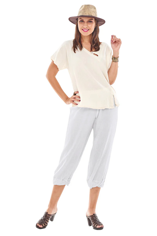 A person wears the "CRYSTAL SNOW" top by Oh My Gauze, a straw hat, and light gray cotton gauze capri pants with tie pocket detail. Smiling with one hand on their hip, they complete the look with dark heeled sandals against a white backdrop.