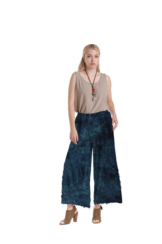A person with long blonde hair stands against a white background, wearing a beige sleeveless top, BENGAL SNOW PANT by Oh My Gauze, tan open-toe heels, and a necklace with a pendant.