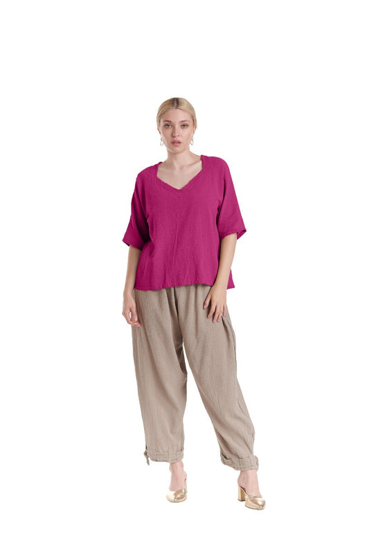 Against a white backdrop, a person dons the ERIN FUCHSIA TOP by Oh My Gauze with loose beige pants and matching shoes. The sweetheart neckline exudes charm as they look towards the camera, hair tied back and expression neutral.