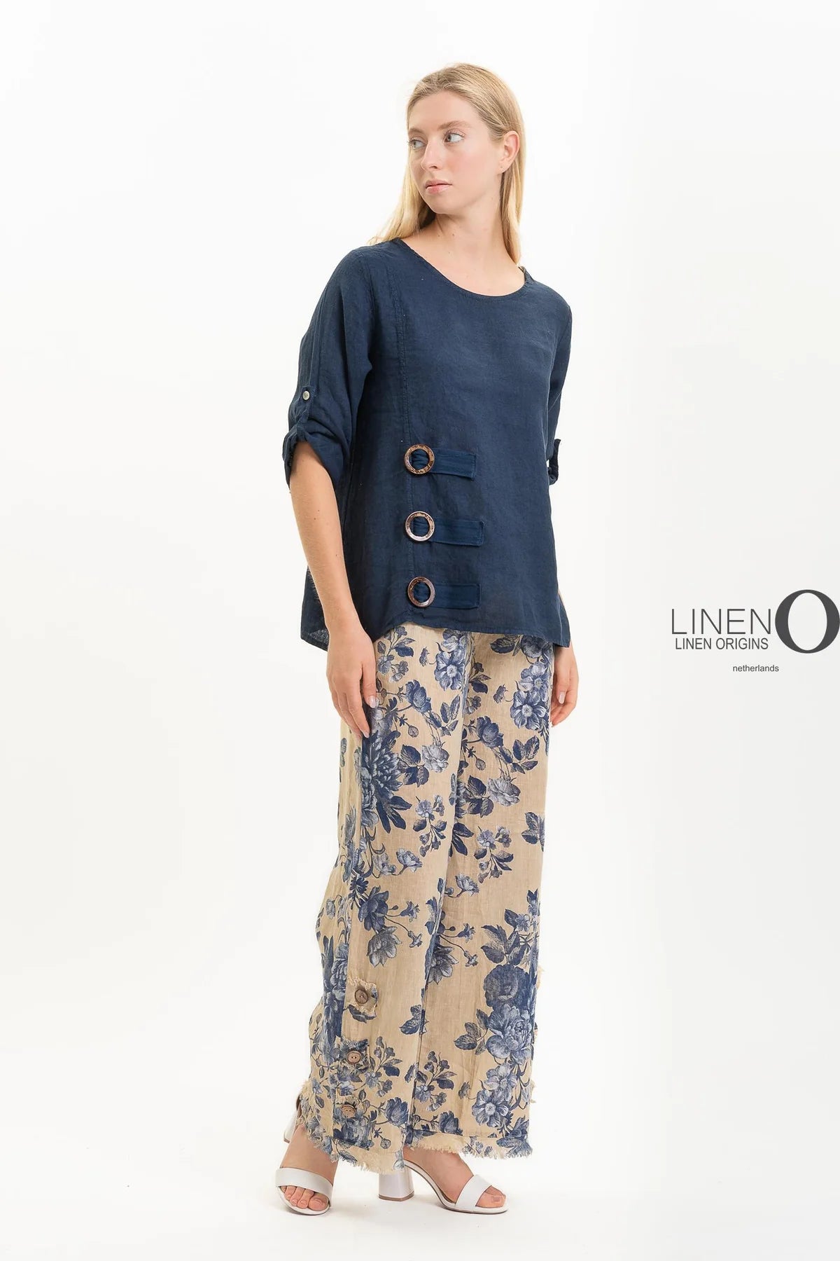 A person poses against a white backdrop in LinenO's French Linen Blouse TP1519-75 Notte and beige wide-leg pants made from eco-friendly European linen with a blue floral design.