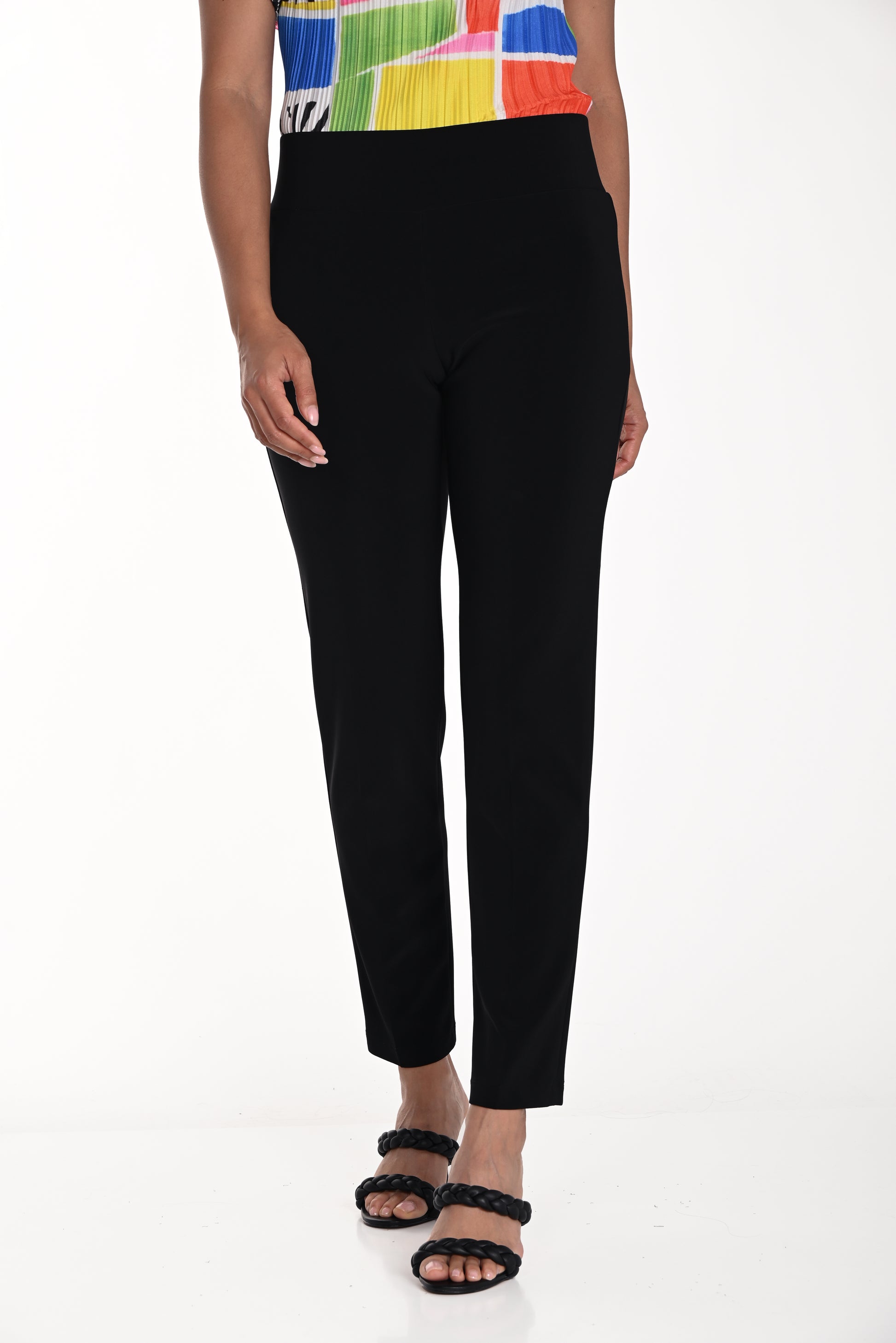 A person, visible from the waist down against a white background, wears the Frank Lyman Slim Leg Pull-On Pant in Black (Style 082)—a stylish Canadian-made pant—paired with a colorful sleeveless top and black braided sandals.