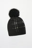 The Joseph Ribkoff Beaded Pom-pom Hat 253969 is a chic black knit beanie with a large faux fur pom-pom, silver studs, and pearls—an elegant winter accessory that stands out against a plain white background.