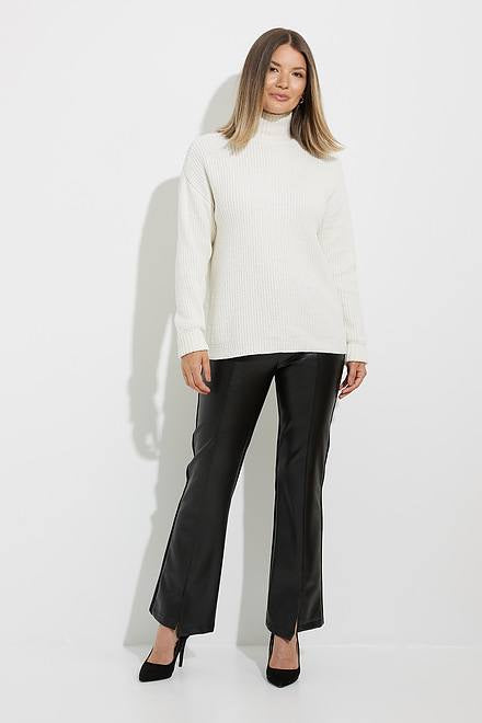 A woman with straight, shoulder-length hair is wearing a white ribbed turtleneck sweater paired with Joseph Ribkoff's Leatherette Pants Style 224311 in black. These pants feature an elastic waist and a flared fit. She completes the look with black heels, standing against a plain white background, looking relaxed with a slight smile.