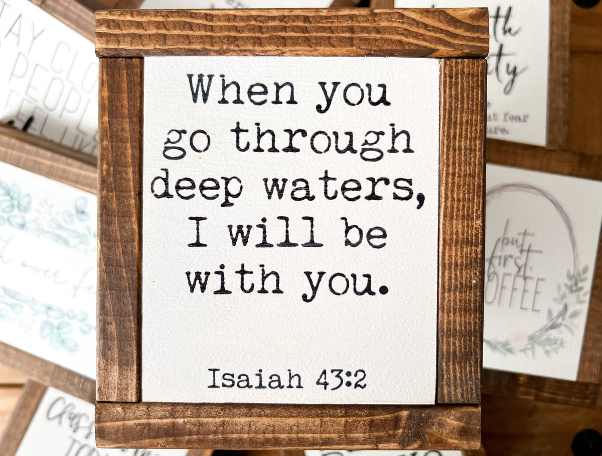 A “Deep Waters mini” wood sign by Inspired Findings, featuring an antique walnut frame, displays the Bible verse Isaiah 43:2: “When you go through deep waters, I will be with you.” Additional mini signs in coordinating frames from Inspired Findings are partially visible in the background.