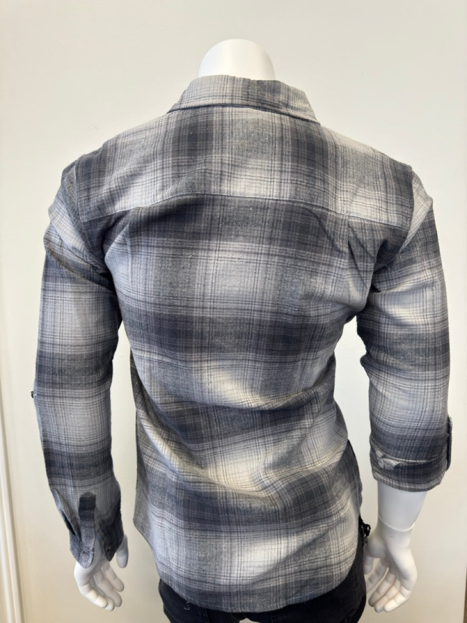 A mannequin dressed in the Silver Jeans Co. Shirt Long Sleeve - GREY, made from 100% cotton and featuring a button-down plaid pattern in shades of black, gray, and white. The shirt includes a collar and a single chest pocket. The mannequin's arms are positioned straight down as it stands against a plain white background.