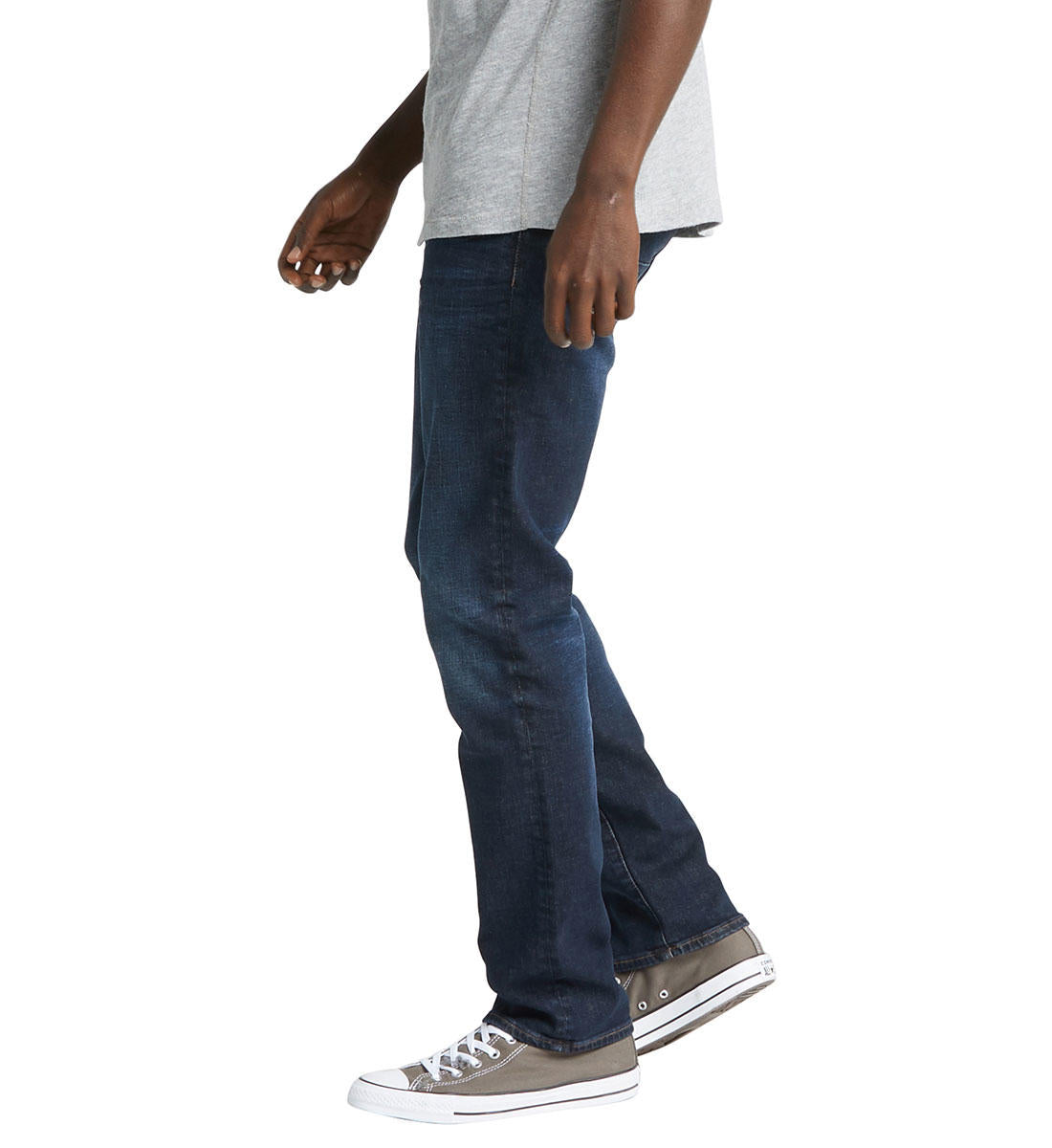 A person wearing a light gray T-shirt, dark blue Machray Classic Fit Straight Leg Jeans by Silver Jeans Co., and gray sneakers is walking. The image captures a side view from the shoulders down, showcasing the casual outfit.