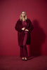 A woman stands against a deep red background, wearing the Joseph Ribkoff Faux Fur Straight Coat 243902F25 with a notched collar over matching flared pants and pointed heels, looking confidently ahead.