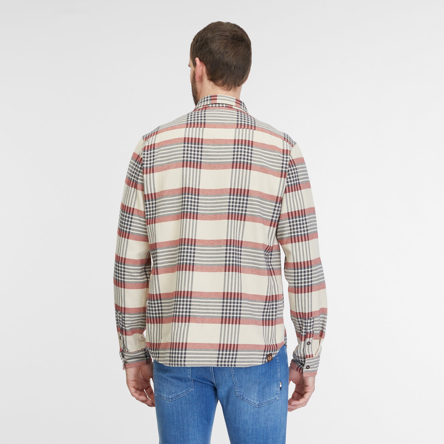 A man with short hair and a beard is standing against a plain white background. He is wearing the Shirt Checki Ecru 2422-40003-7004 by RAGWEAR, featuring a beige, red, and black plaid pattern made from vegan streetwear-inspired cotton flannel, paired with blue jeans. He is looking directly at the camera with a neutral expression.