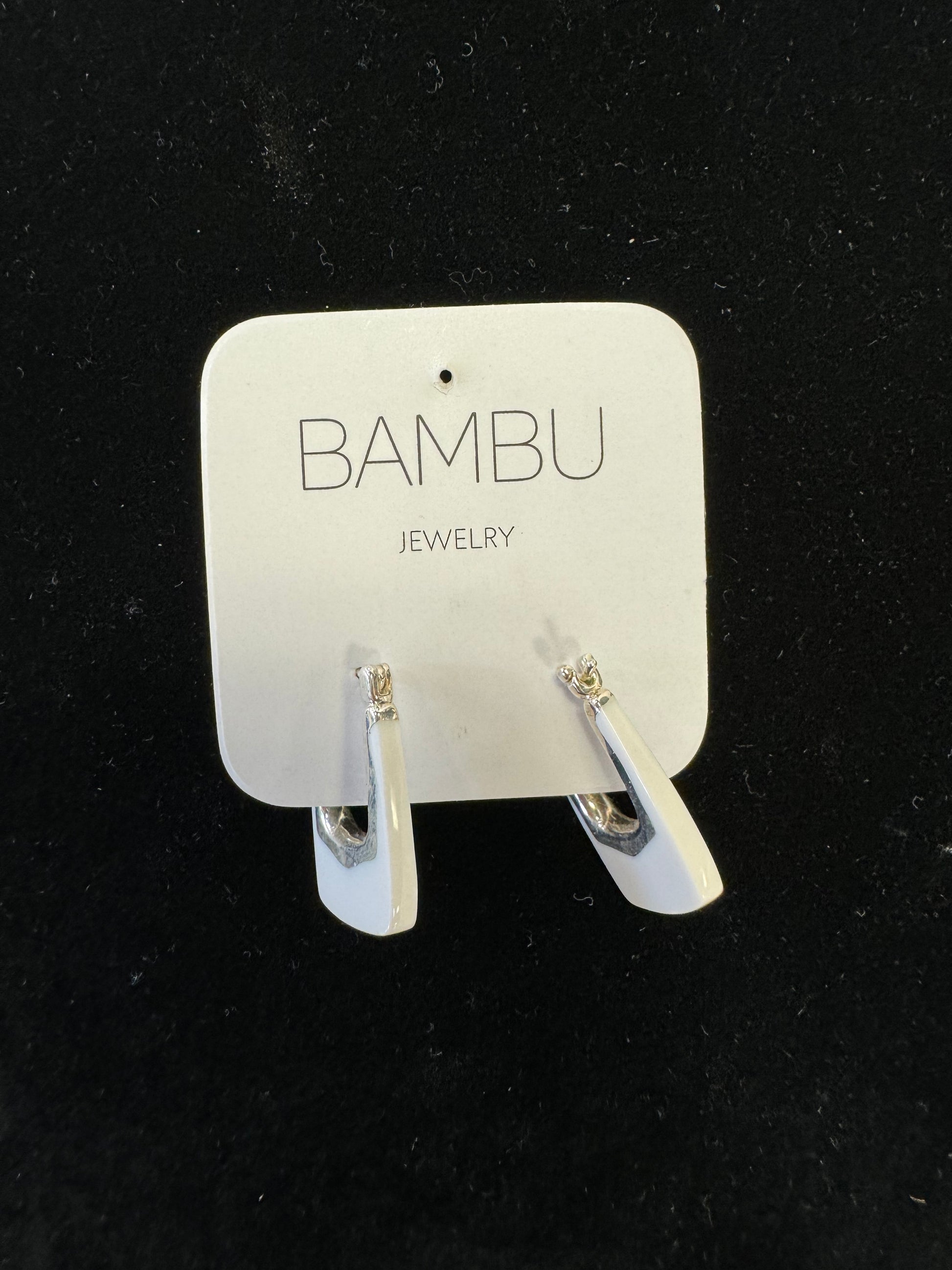 A pair of White & Silver Earring - BAMBU on a white card labeled "BAMBU Jewellery." These elegant accessories feature a sleek, triangular design with a small, clear gemstone at the top. The card and earrings are set against a black background.