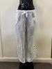 White linen pants (Pants Linen White 4406 - Bella Amore) displayed on a black mannequin against a plain backdrop. These 100% linen pants, crafted in Italy by Bella Amore, feature a drawstring waist and button details at the hems.