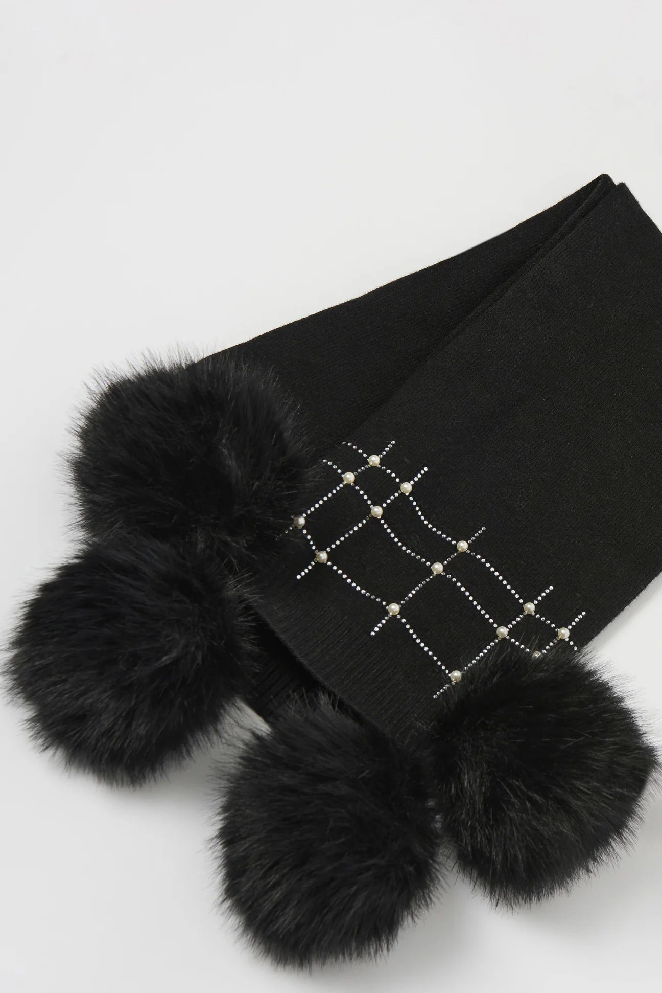 The Joseph Ribkoff Knitted Faux Fur Pom-Pom Scarf 253970 features a black crisscross stud pattern and large, fluffy faux fur pom-poms at each end—perfect to pair with your favorite Joseph Ribkoff beanie.