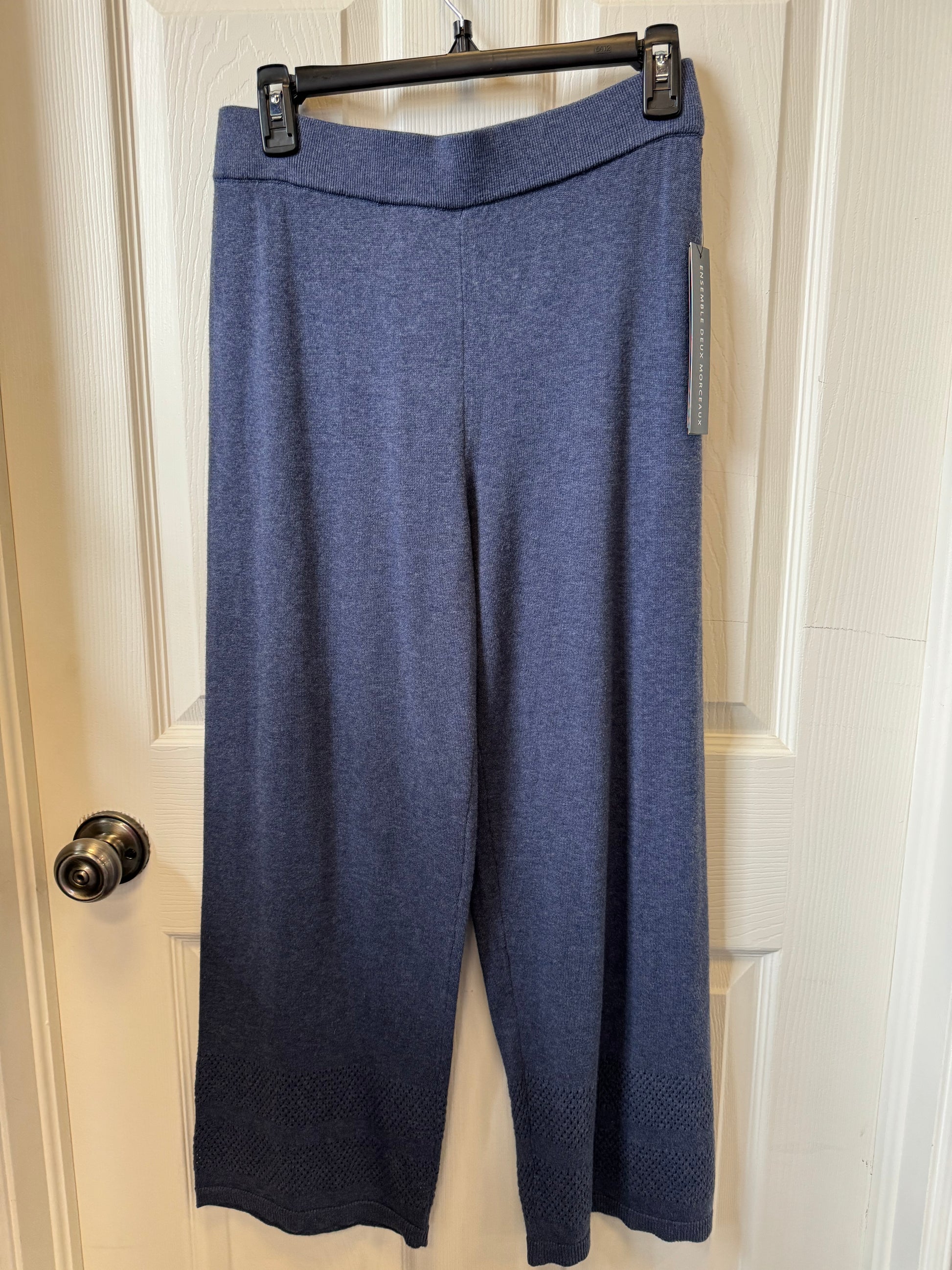 A pair of versatile Tribal Dark Navy Casual Pants - 4828O-576-0657 hangs on a black plastic hanger attached to a white door. The full-length pants, made by the brand Tribal from 100% cotton, feature a straight cut design with subtle patterns near the hem. The door has a silver doorknob on the left side.