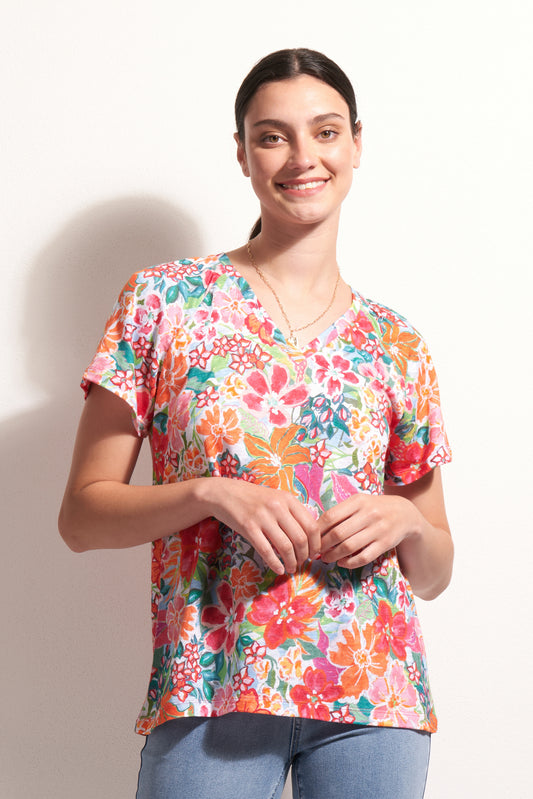 A smiling woman with dark hair tied back wears the FOIL Sew Cute Top FO8246 Island Time, a breathable, short-sleeved knit linen top with an island-inspired print, paired with light blue jeans against a white background.