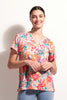 A smiling woman with dark hair tied back wears the FOIL Sew Cute Top FO8246 Island Time, a breathable, short-sleeved knit linen top with an island-inspired print, paired with light blue jeans against a white background.