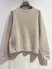 A beige “Round-neck sweater 70% alpaca 8028” by NOELINE hangs on a black hanger against a white wall.