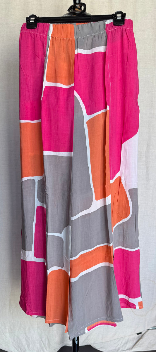 The TaraVao Pant Maora 4016 features a bold geometric pattern in pink, orange, gray, and white on lightweight rayon, displayed on a black hanger against a light background.