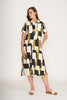 A woman stands against a plain background wearing the FOIL Advanced Interaction Dress Art Box FO8296, a short-sleeve, button-up linen dress featuring a bold black, white, and mustard yellow print, styled with white sandals.