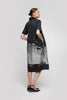 A person with short brown hair showcases the stylish and comfortable SHORT SLEEVE SHIRT DRESS WITH TROMPE L'OEIL PRINT by UCHUU, featuring a graphic design and flowy silhouette. They stand sideways in black flat shoes against a plain gray background.