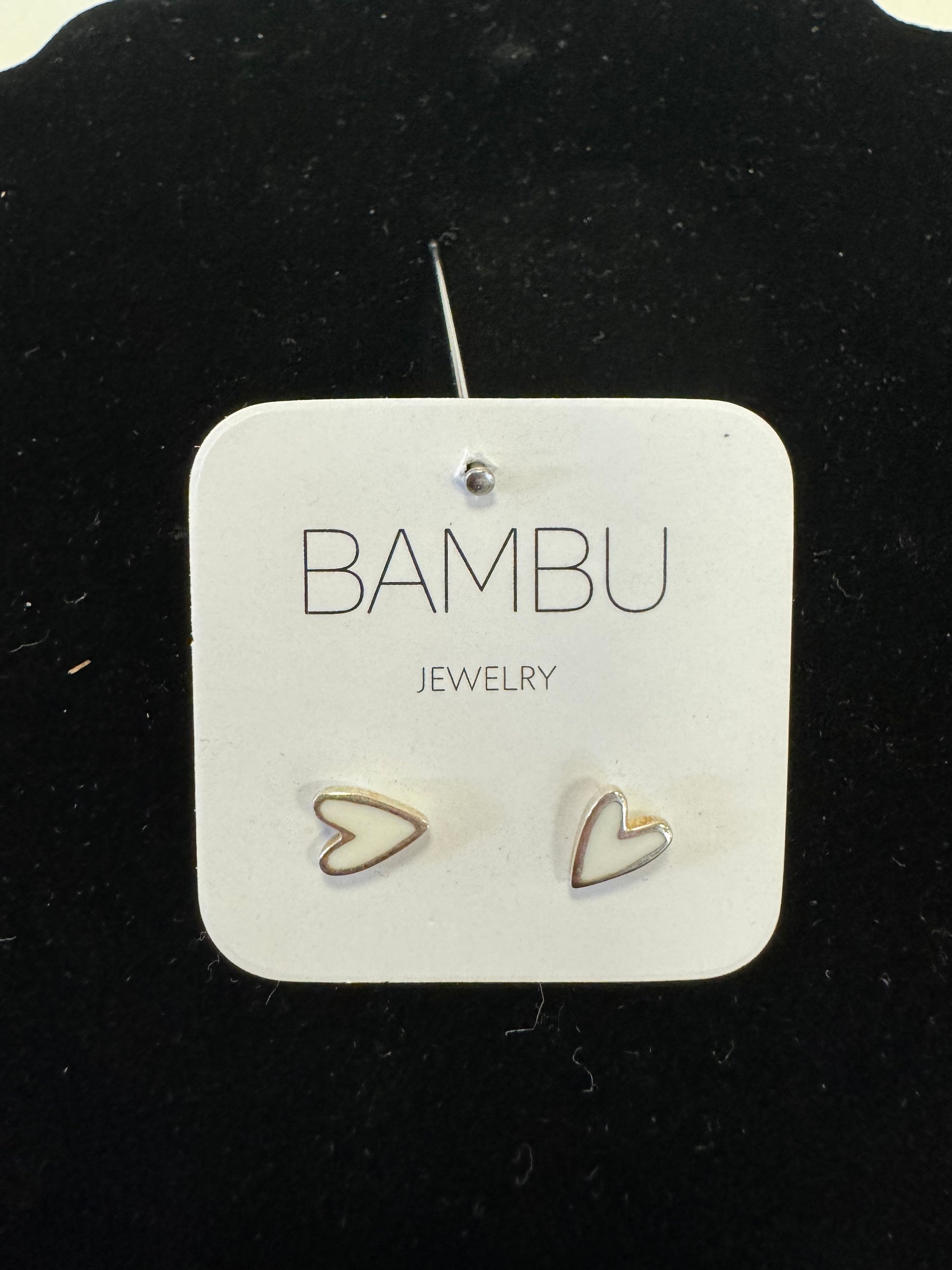 A jewelry card featuring the brand name "BAMBU Jewellery" and the word "JEWELLERY" below it showcases a pair of small, heart-shaped stud earrings from the White Silver Gold - BAMBU collection. One earring is solid, while the other features a cutout design. The elegant card is set against a black background with a subtle gold border.