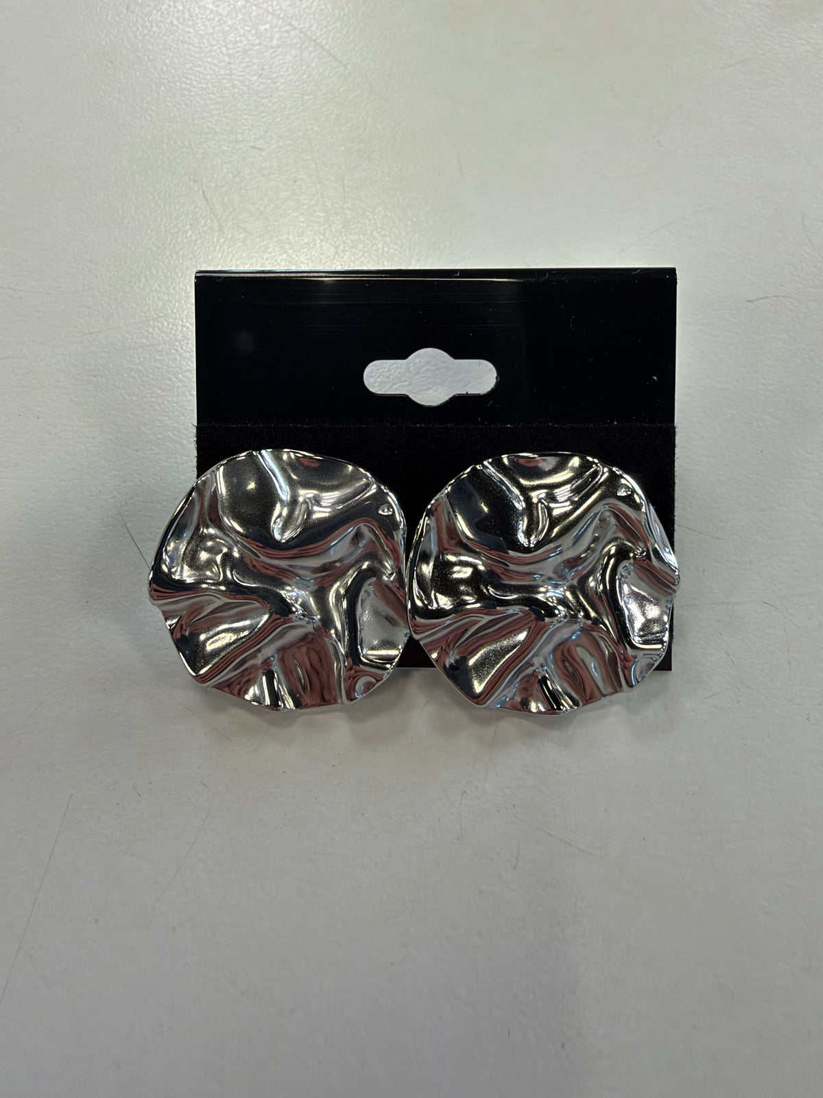 Pair of silver-toned hammered round Dior 11 Earrings with a wavy, rippled surface, displayed on a black earring card.