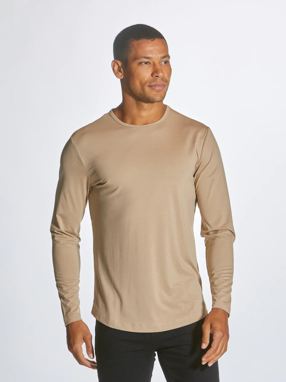 A beige AO Long Sleeve Curve-Hem tee is laid flat on a white background. This signature-fit t-shirt by CUTS features a simple design with a rounded neckline and is crafted from PYCA Pro fabric. A small tag near the collar displays the brand name, "CUTS".