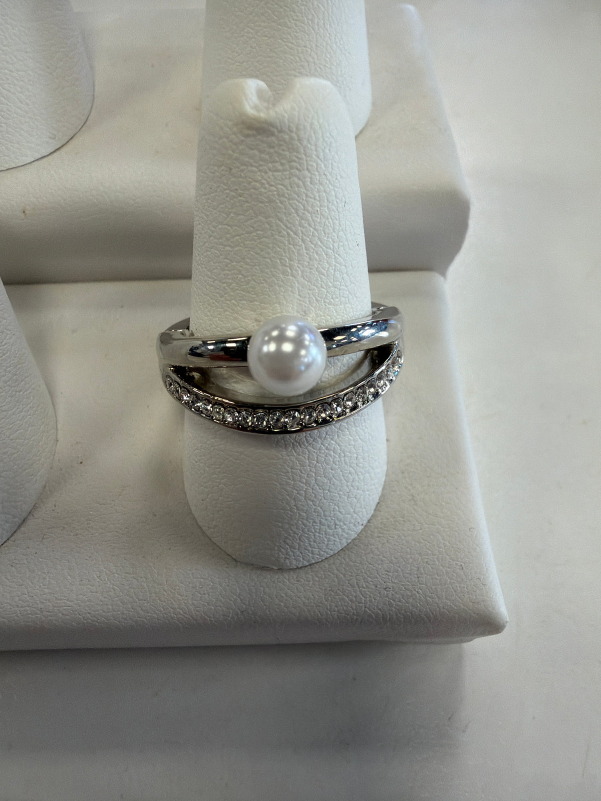 Jenna 72 Ring by Elise accessories featuring a double band with a center pearl on one band and a row of sparkling CZ stones on the other, displayed on a ring stand.