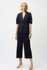 A woman poses against a plain background in Joseph Ribkoff’s Culotte Jeans With Exposed Side Zipper 261955, styled with a modern denim blazer, gold heels, and simple jewelry.