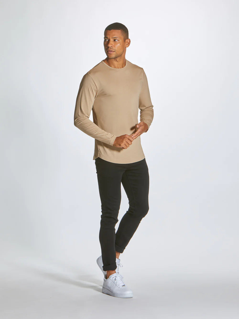 A beige AO Long Sleeve Curve-Hem tee is laid flat on a white background. This signature-fit t-shirt by CUTS features a simple design with a rounded neckline and is crafted from PYCA Pro fabric. A small tag near the collar displays the brand name, "CUTS".