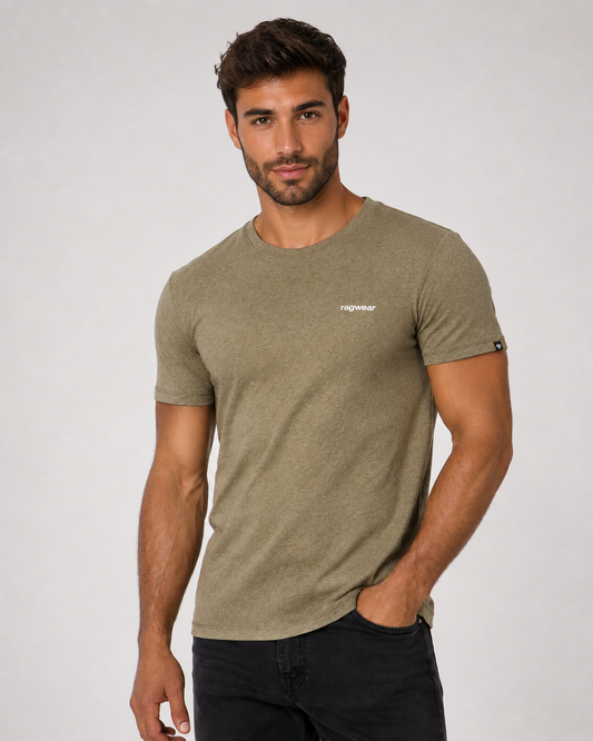 A man with short brown hair and a beard wears the RAGWEAR Hallys Tee 2612-15004 in Dark Olive, featuring a small white chest logo, paired with black jeans. He stands against a light background, one hand in his pocket.