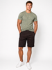 A man stands against a white background, wearing a light green patterned t-shirt, Silver Jeans Co. Ashton Stretch Twill Walking Shorts in black, and white sneakers. His hands are in his shorts pockets and he looks directly at the camera.