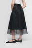 A person in a white top and the UCHUU SKIRT WITH MESH PETTICOAT, CS25-203, stands with their back to the camera. They wear black pointed flats with ankle straps in a simple, light setting that highlights UCHUU Montreal's minimalist elegance.