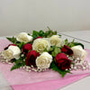 The 1 Dozen Red & White Roses Freshcut by Posies Flowers & Fashion is elegantly arranged on pink tissue paper, featuring lush green leaves and tiny white flowers, all set against a plain white background.