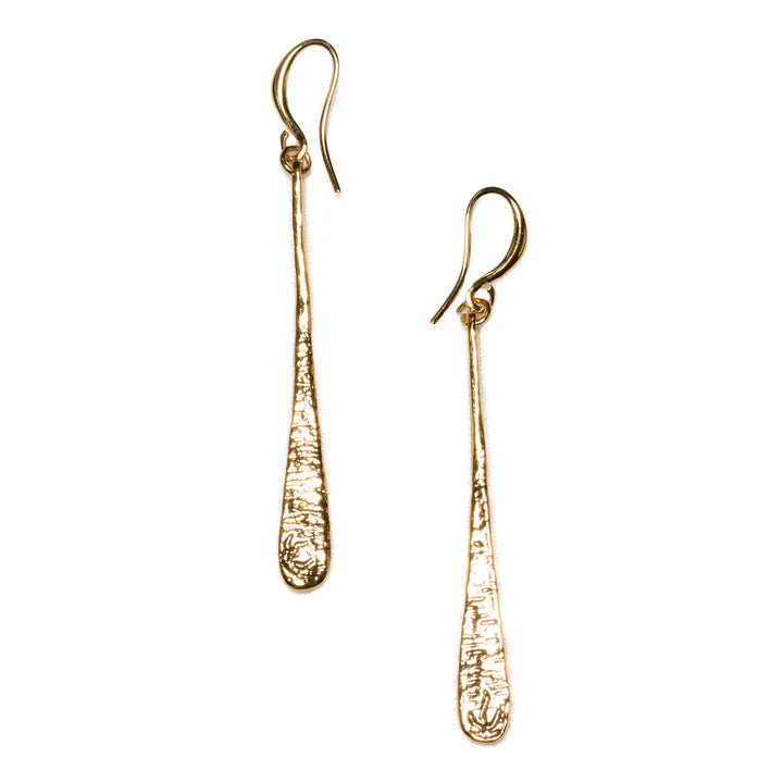 Two long, textured gold dangle earrings with hook clasps. Each earring has a slender, tapered design with a slightly widened end, displaying a rough, hammered surface. These Bali-inspired pieces of handmade jewellery are crafted from ethically sourced materials. The **Beaten Tear Drop Earrings - Gold Plate** by **Suzie Blue** are truly stunning.