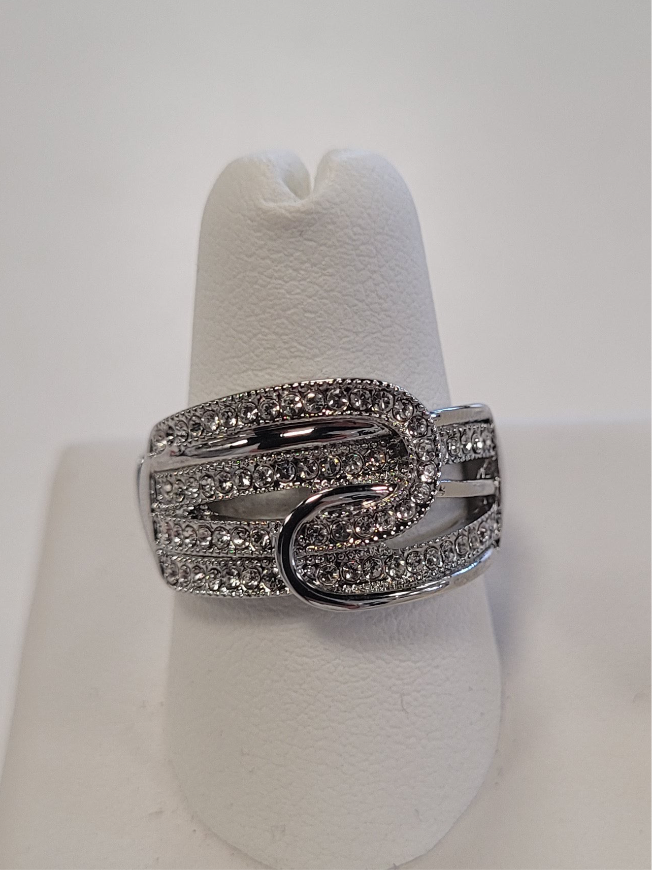 The JENNA-75 Adjustable Ring by Elise accessories features interlocking silver loops in a fold-over rope design, embellished with sparkling white stones, shown on a white ring stand against a plain background.