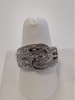 The JENNA-75 Adjustable Ring by Elise accessories features interlocking silver loops in a fold-over rope design, embellished with sparkling white stones, shown on a white ring stand against a plain background.