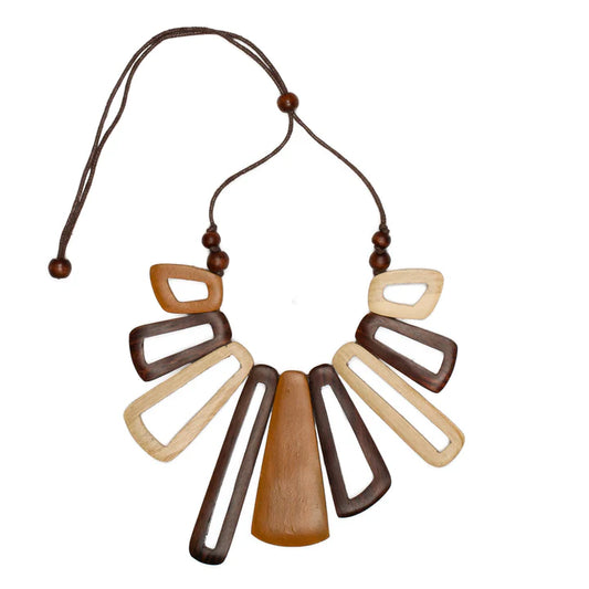 The Suzie Blue Short Tinted Wood Fan Necklace is a handcrafted, handmade necklace showcasing large geometric wooden pieces in dark brown and light tan shades. It features an adjustable cord with wooden bead accents, and its blend of solid and open rectangular shapes makes for a striking statement piece that's sure to impress.