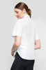 A person with brown hair tied back, in an UCHUU SHORT-SLEEVED SHIRT WITH WAVY RUFFLES CS25-602, and black pants, facing sideways against a gray background.
