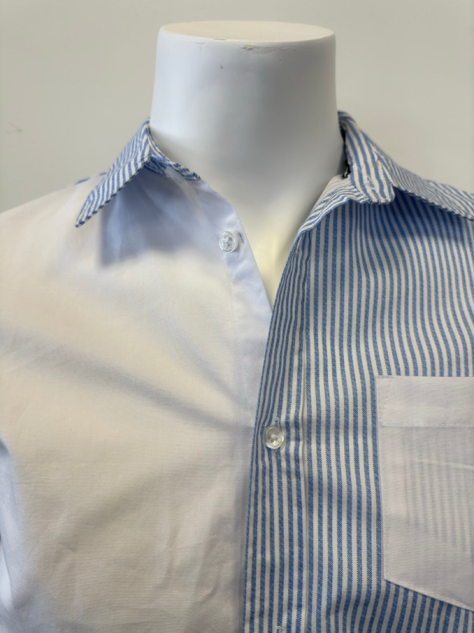 A mannequin showcases the Men’s Cotton Shirt - STRIPE WHITE/BLUE by Silver Jeans Co., which features a button-up style with alternating vertical white and blue stripes on the right side and pocket. The left side and sleeves are solid white, prominently displayed against a plain backdrop that accentuates the garment's unique design.