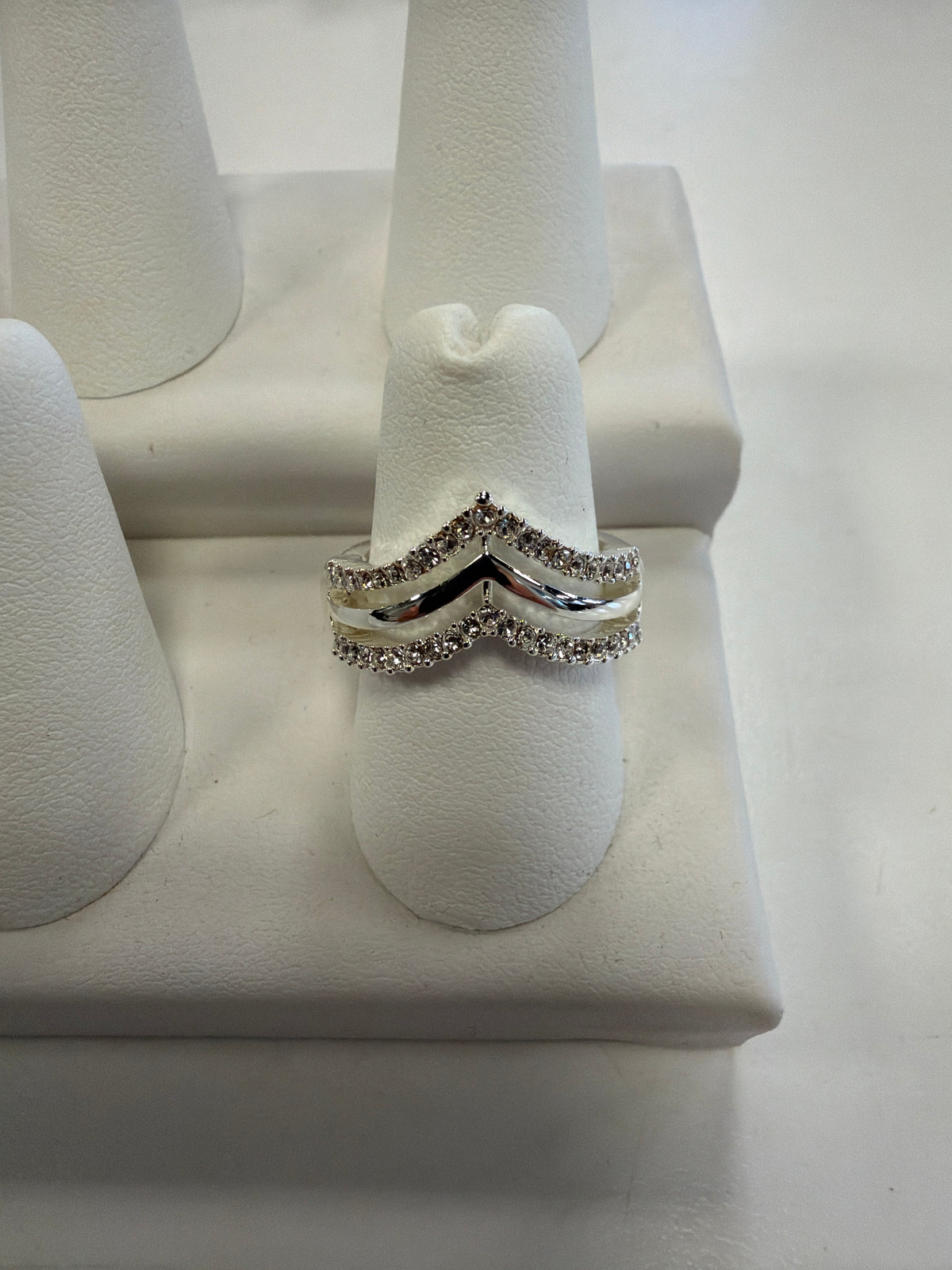 Jenna 81 Ring, a silver double chevron ring set with small clear CZ stones, displayed on a white ring stand.