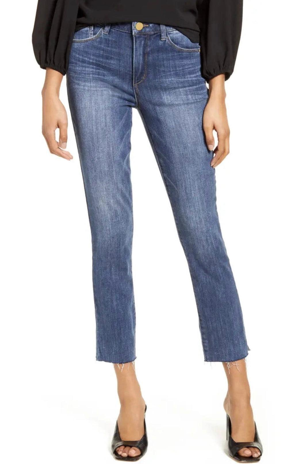 A person is wearing dark blue, slightly faded Logan Hi-Rise Skinny L1557KF8 jeans from Wit & Wisdom featuring a frayed hem and a black long-sleeve top. They are also sporting black high-heeled shoes. The image, which appears to be styled by Nordstrom, focuses on the clothing from the waist down.