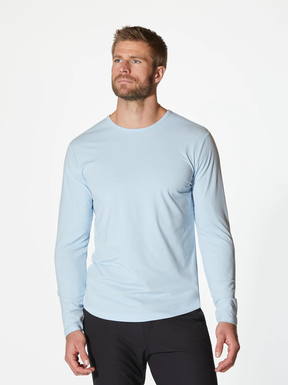 A light blue AO Long Sleeve Curve-Hem Tee by CUTS showcases a simple and clean design. This Signature-fit piece features a small black tag with white text near the neckline inside the back, and a small black X logo stitched near the bottom left side. Made from PYCA Pro fabric, it feels soft and smooth to the touch.