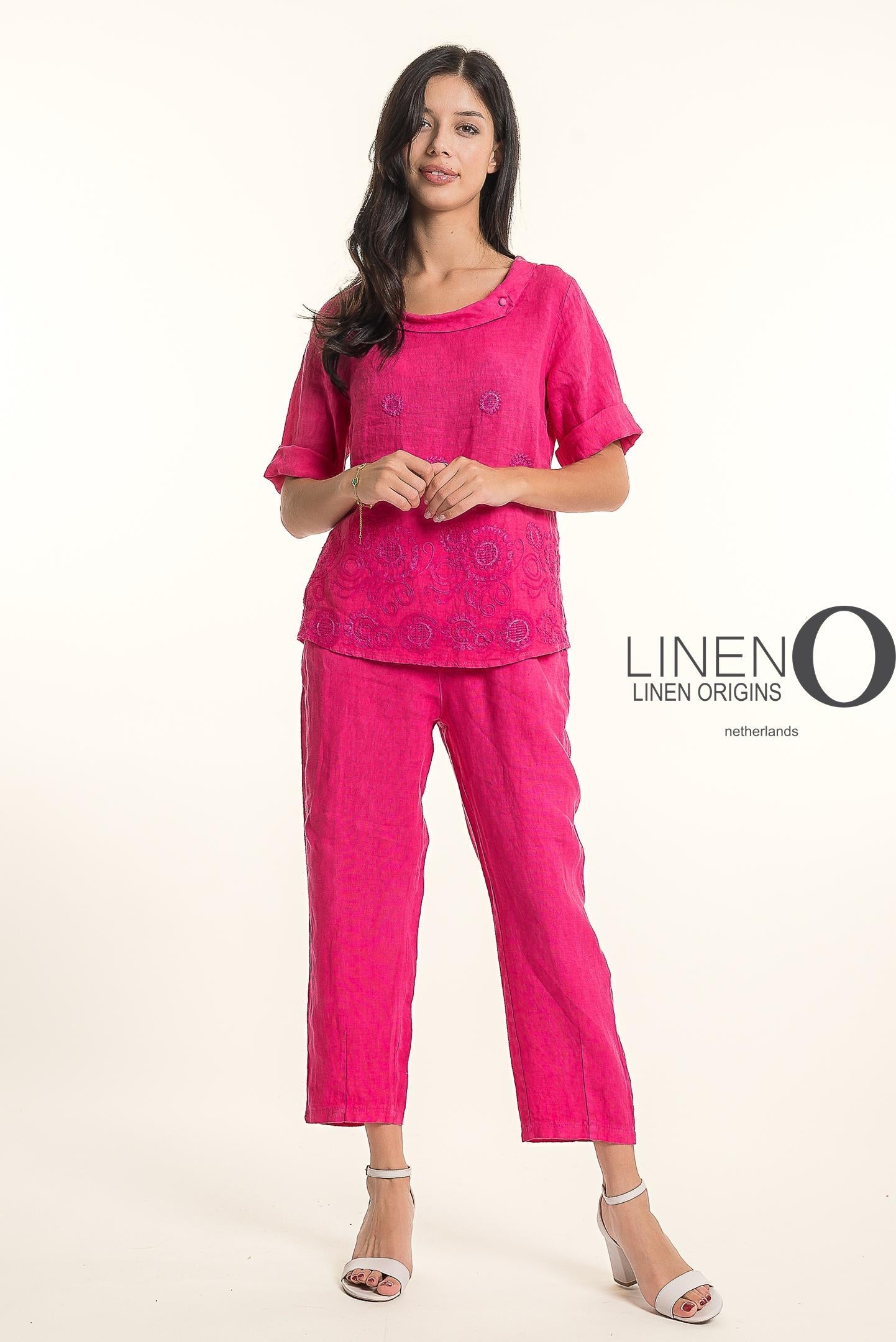 A woman with long dark hair wears the LinenO French Linen Blouse TP1743-43 in Fuxia, paired with matching pants and white heeled sandals, standing against a plain background. The words "LINEN ORIGINS" appear beside her.