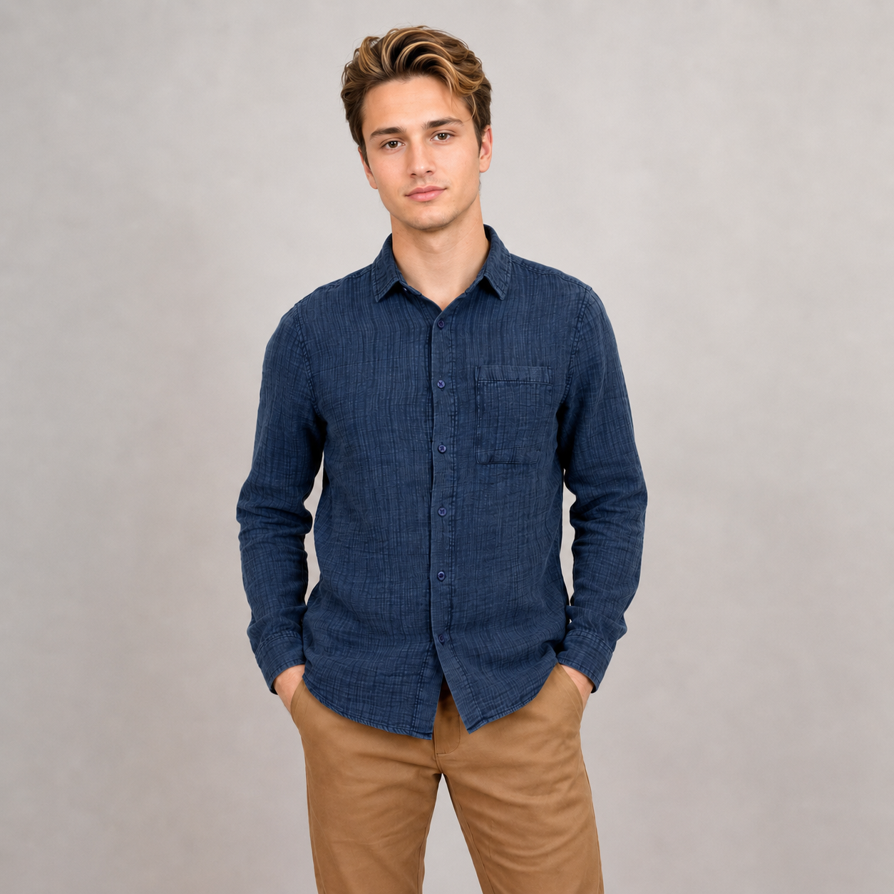 A young man with light brown hair wears the HEDGE Gauze Long Sleeve Shirt Navy (56MW102S) and tan pants, standing with hands in pockets against a plain light gray background—ideal for your summer wardrobe.
