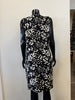 A sleek black mannequin displays Bali Corp.'s Dress 8555, a sleeveless, knee-length design featuring a white leaf pattern and crafted from 100% viscose, set against a minimal indoor backdrop.