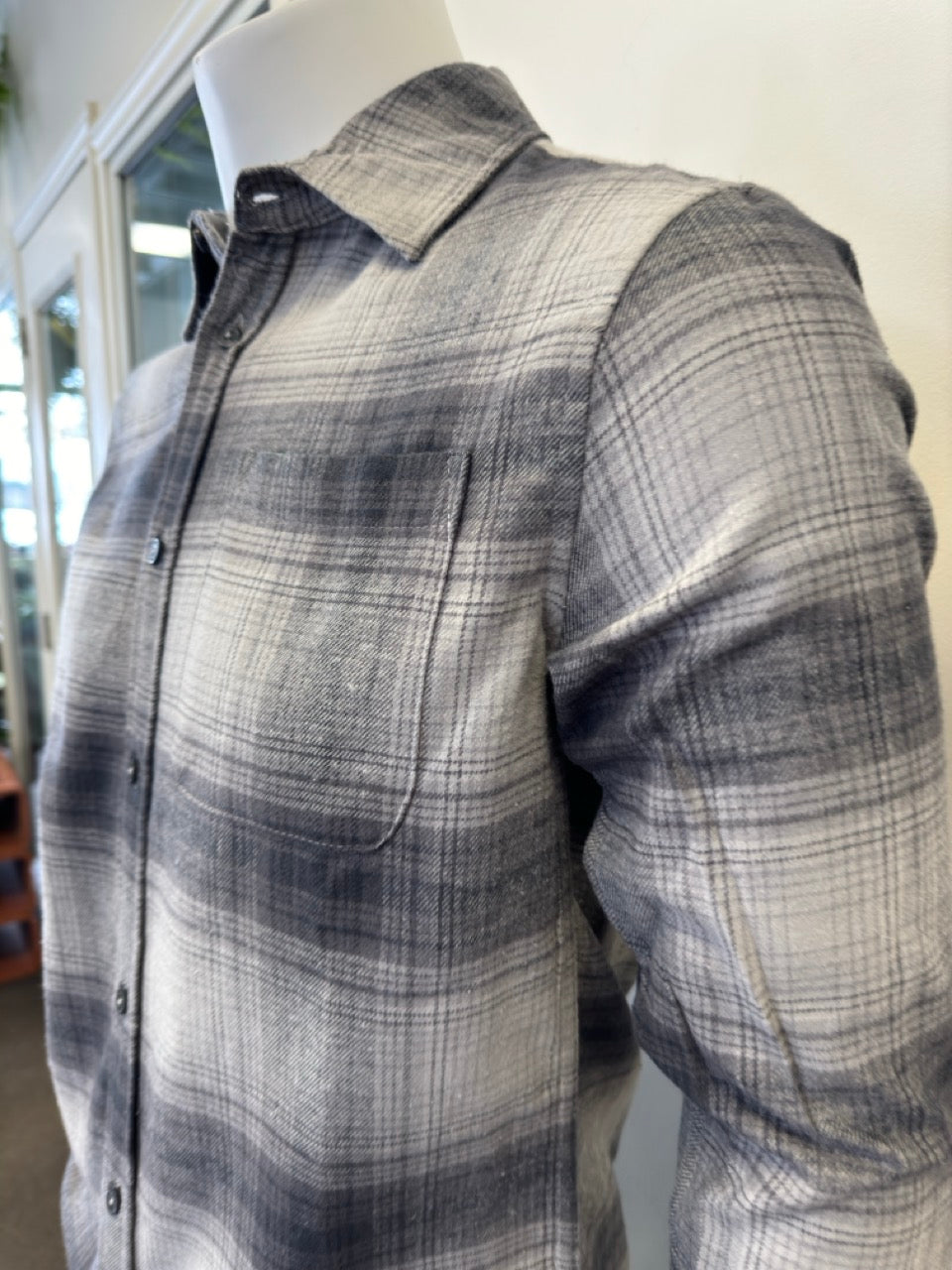 A mannequin dressed in the Silver Jeans Co. Shirt Long Sleeve - GREY, made from 100% cotton and featuring a button-down plaid pattern in shades of black, gray, and white. The shirt includes a collar and a single chest pocket. The mannequin's arms are positioned straight down as it stands against a plain white background.