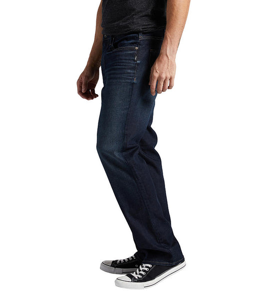 A person wearing Allan Slim Fit Straight Leg Jeans by Silver Jeans Co., a dark shirt, and black-and-white sneakers stands against a plain white background. The person's arms hang naturally by their sides, with the left arm slightly bent. Only the lower half of the body is visible.