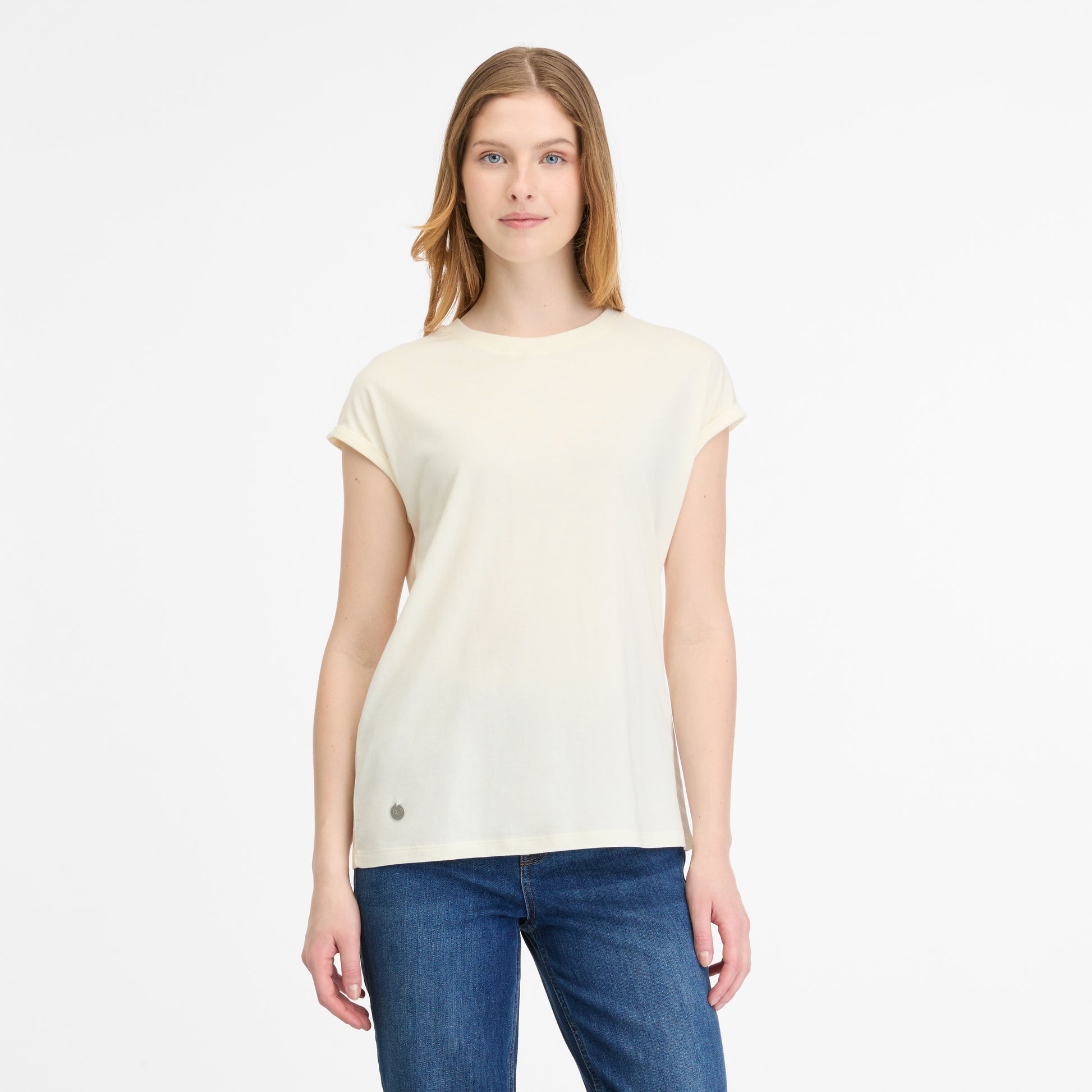 Long-haired woman in blue jeans wears a DIONA A T-SHIRT by RAGWEAR, off-white and vegan, against a white backdrop.