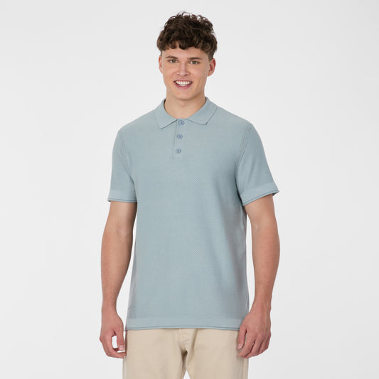 A young man with short brown hair smiles while wearing a RAGWEAR Polo Tarsh Short 2612-15050-2046 in dusty blue and beige pants, standing against a plain white background.